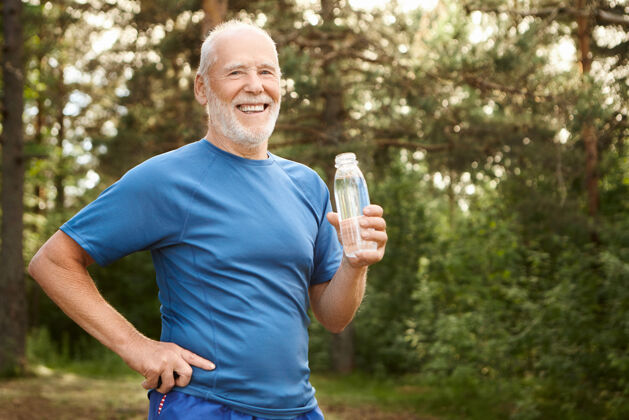 肖像一幅快乐活泼的白种退休老人的画像 他留着胡子 大胆的头 手放在腰上 喝着玻璃瓶里的淡水 早上在公园里锻炼身体后休息60多岁健身退休