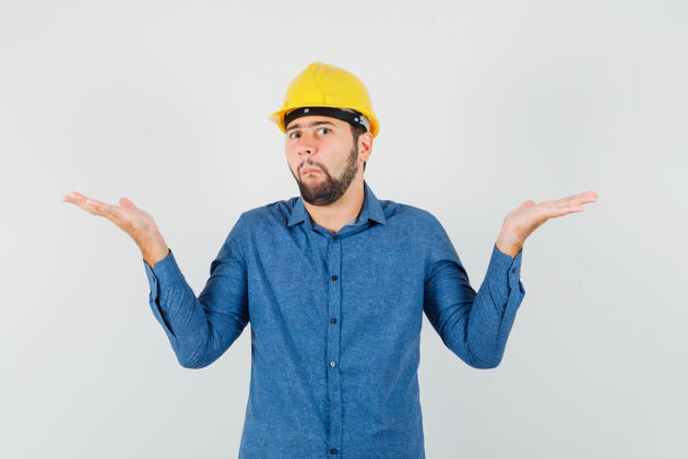 会议年轻工人穿着衬衫 戴着头盔 表现出无助的姿态 看上去很困惑伙伴关系职业工程师