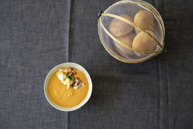 室内头顶特写镜头的橙色汤汁在一个白色的碗与面包上的黑色桌布食物健康勺子