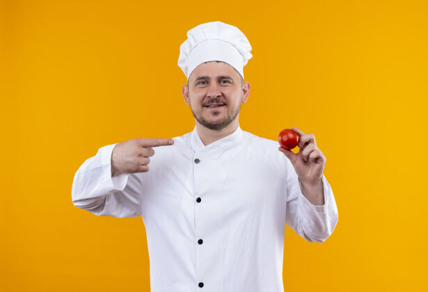 厨师身着厨师制服的年轻帅哥面带微笑 手拿西红柿 指着橘黄色的空间厨师西红柿指着