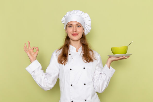 食物身着白色厨师服的女厨师微笑着拿着绿色的盘子站在绿色的墙上衣服举行淋浴