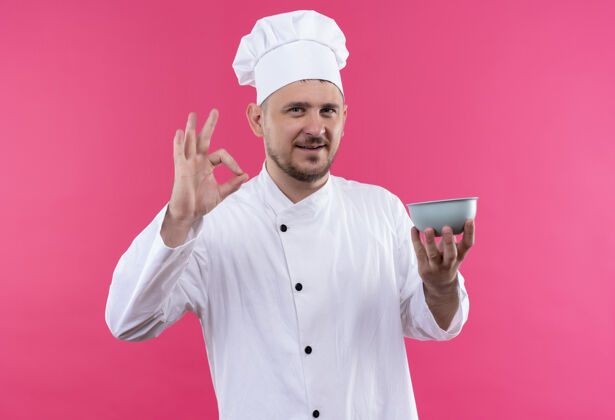 制服微笑的年轻帅哥厨师穿着厨师制服拿着碗做ok标志孤立在粉色空间厨师烹饪帅气