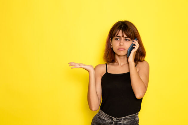 情绪身穿黑衬衫的年轻女性在浅黄色墙上讲电话的正面视图性感前面说话