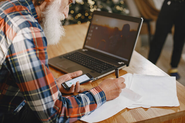 家老人拿着笔记本电脑爷爷坐在圣诞装饰品里老人拿着手机网络家庭成人
