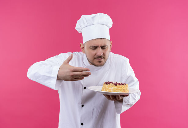 盘子穿着厨师制服的年轻帅哥厨师拿着一盘蛋糕 在粉色的空间里嗅着它年轻拿着粉色