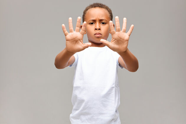 男孩一幅严肃的美国黑人小男孩的画像 他穿着白色t恤 皱着眉头 表情暴躁 双手十个手指都没有做任何手势或停车标志肖像手指休闲