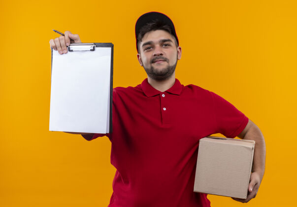 盒子年轻的送货员穿着红色制服 戴着帽子 拿着一个盒子 里面有空白页的剪贴板 要求签名签名红色包装