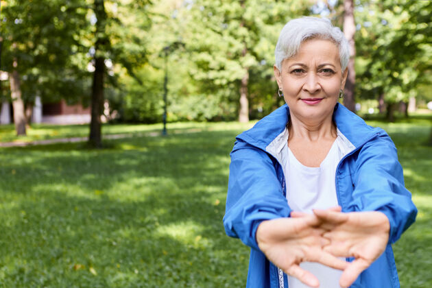 老年人运动型的退休女性穿着时尚的运动服 在户外伸展双手肌肉训练 做瑜伽练习 保持良好的身材快乐的成熟女性退休者伸出双臂活动成熟退休