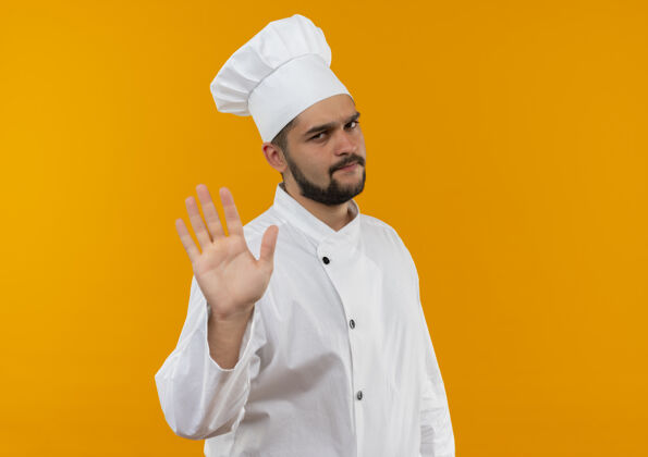 男性穿着厨师制服的年轻男厨师站在橙色的空间里做手势停止厨师橙色