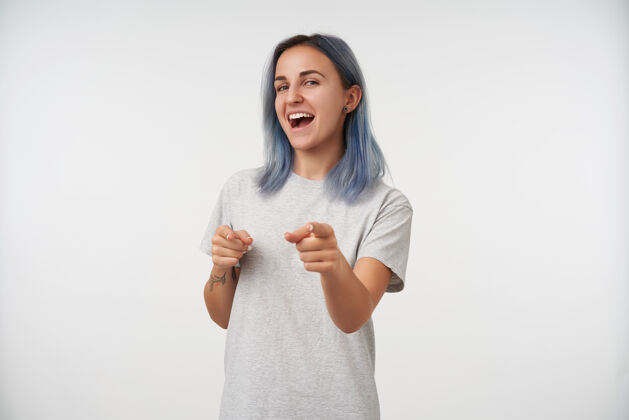 化妆品年轻快乐的纹身女士的肖像 蓝色短发举起双手 用食指快乐地展示 孤立于白色显示自然基本
