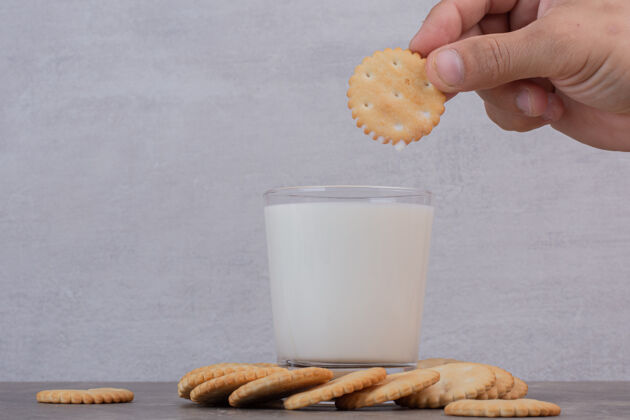 玻璃男人的手拿着一块饼干放在大理石桌上的牛奶上面小吃小麦牛奶