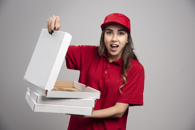 女性身着红色制服的女信使在灰色的墙上拿着一个小披萨盒披萨表情女人