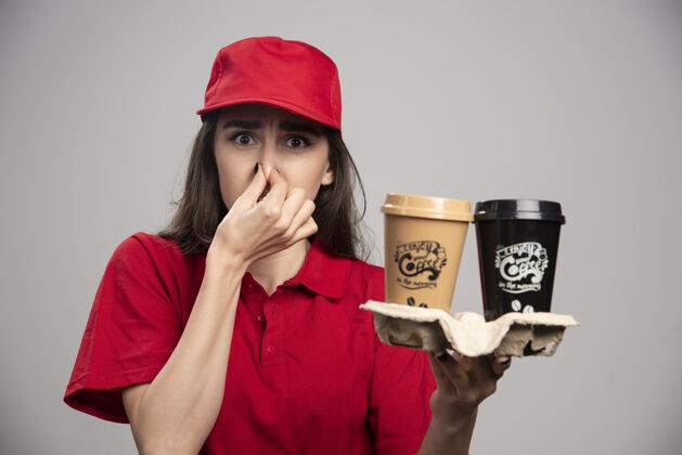 女孩一个穿着红色制服的女送货员因为闻到气味而紧紧地捏着鼻子工作女人杯子