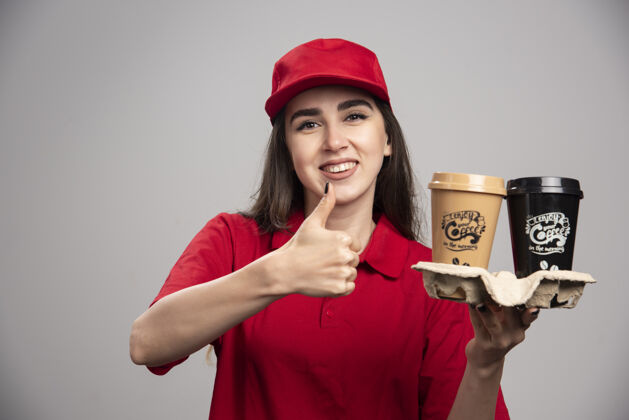 送货穿着红色制服的送货员拿着咖啡杯 竖起大拇指职业工作杯子