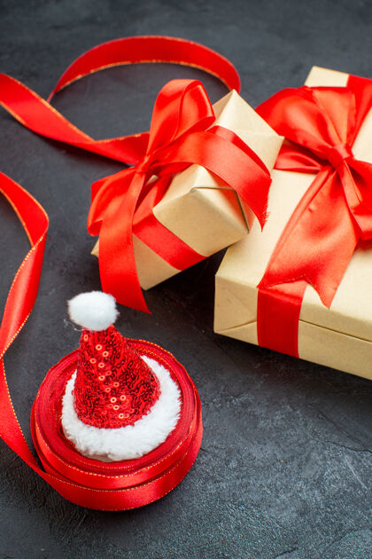 圣诞老人黑色桌子上的红色丝带和圣诞老人帽子的美丽礼物的垂直视图风景帽子蝴蝶结