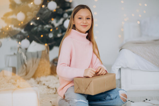 雪可爱的女孩拿着圣诞礼物在圣诞树旁积极毛衣可爱