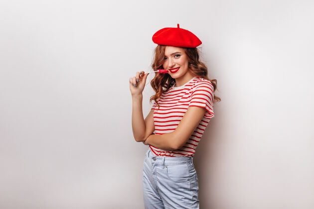 年轻身着红色贝雷帽手持糖果的热情女模特兴奋的白人女孩和棒棒糖Swoosh迷人玩