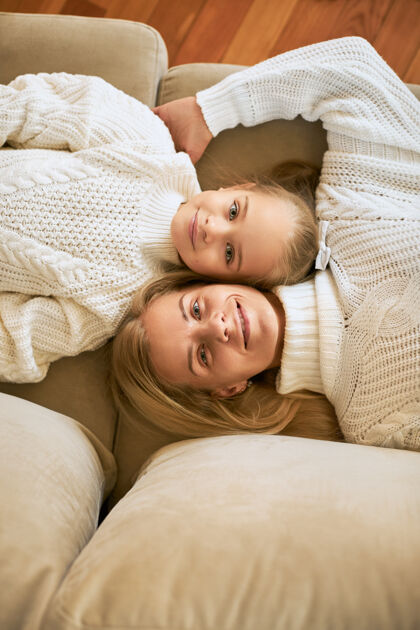 微笑幸福家庭在家放松的俯视图美丽的年轻母亲和她可爱的女儿头对头地躺在沙发上 幸福地微笑着 穿着毛衣的垂直镜头享受坦诚快乐