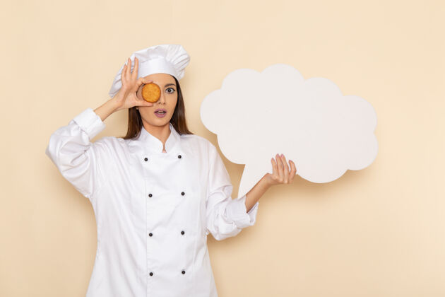 前面身穿白色厨师服的年轻女厨师的正面图 白色墙上拿着白色的牌子和饼干专业人肖像