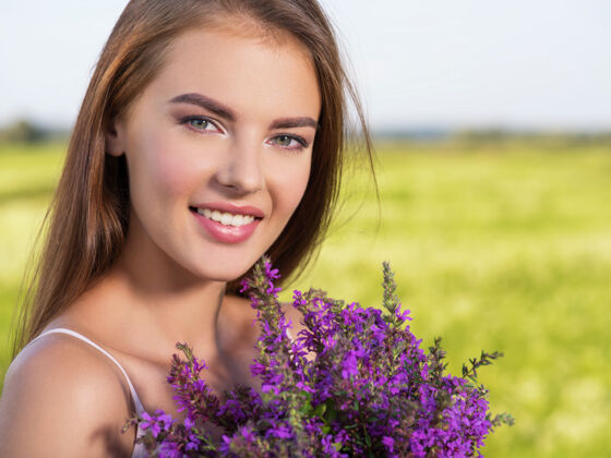 性感快乐微笑的美丽女子 手拿紫花 在户外年轻开朗的女孩 在大自然的春天田野上自由概念草地上一位美丽性感模特的肖像女性欢乐田野