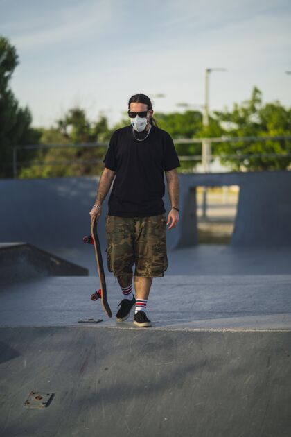 滑板戴着医用面罩的滑板在公园里行走的年轻男性-covid-19概念男孩设备健身