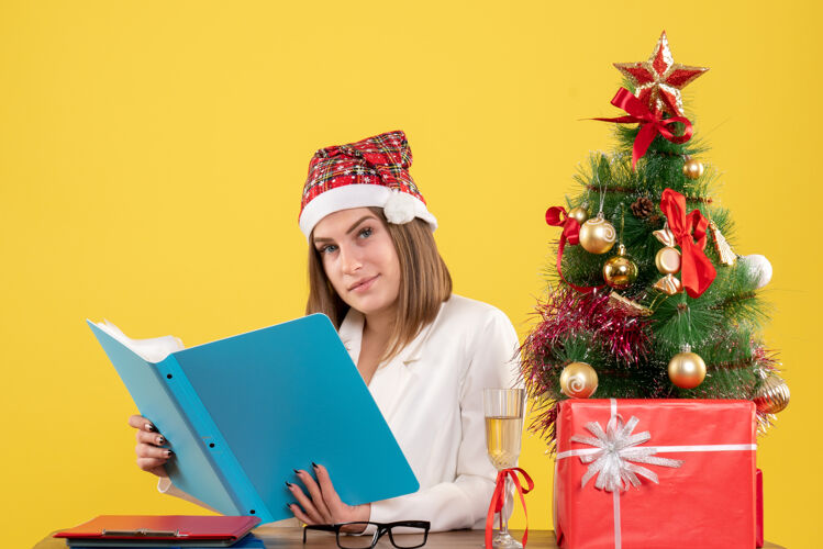商务前视图女医生坐在圣诞礼物持有黄色背景文件礼物前面工作