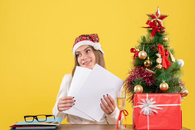 工作前视图女医生坐在圣诞礼物拿着黄色背景上的文件人快乐健康