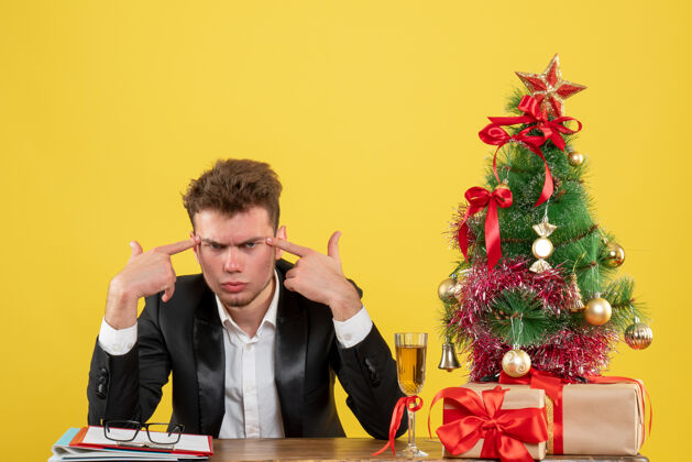 圣诞节正面图：男员工坐在黄色办公桌上的工作台后面 情绪激动 办公室工作 新年快乐工人颜色情侣