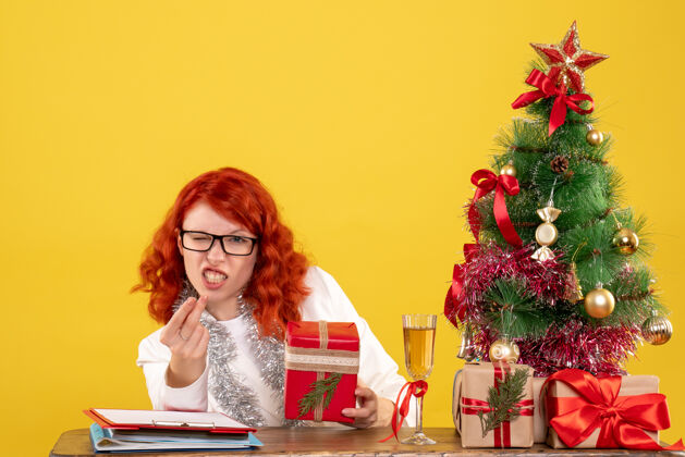 桌子前视图：女医生坐在桌子后面 黄色背景上有圣诞礼物情感安排成人