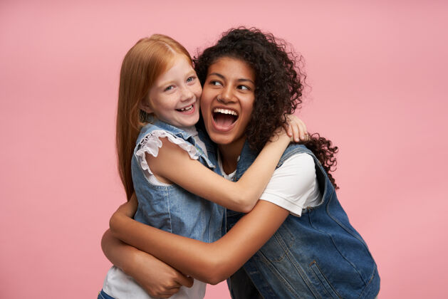 拥抱两个年轻开朗的女孩 穿着家庭装 站在粉色的床上 一起开心地笑着皮肤表情年轻