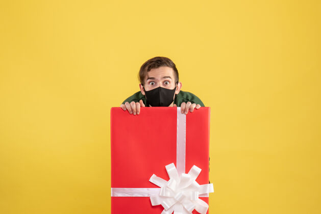 购物正面图戴着面具的大眼睛男人藏在黄色的大礼品盒后面面具包徽章