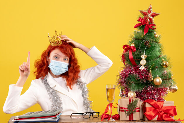 圣诞节前视图：女医生带着圣诞礼物坐着 戴着黄色背景的皇冠性感情感女性