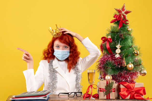 快乐前视图：女医生带着圣诞礼物坐着 戴着黄色背景的皇冠女性背景礼物
