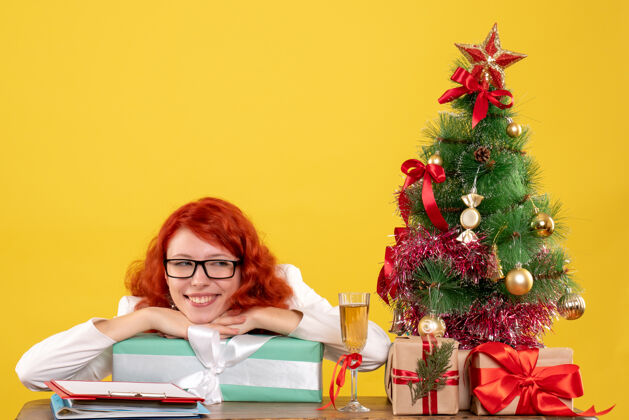 背景前视图：女医生拿着圣诞礼物和黄色背景上的圣诞树坐着花礼物礼物
