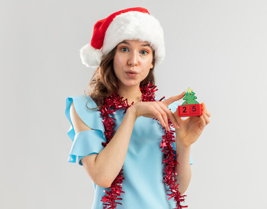 金属片身穿蓝色上衣 戴着圣诞帽 脖子上戴着金属丝的年轻女子 手里拿着玩具立方体 圣诞节的日子看起来很快乐 笑容满面周围年轻立方体