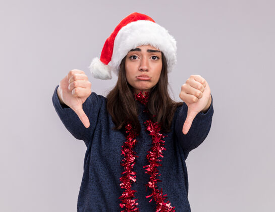 拇指失望的白人女孩戴着圣诞帽 脖子上戴着花环 大拇指朝下失望年轻快乐