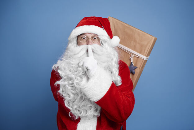 手指放在嘴唇上圣诞老人背着圣诞礼物分享站着礼物