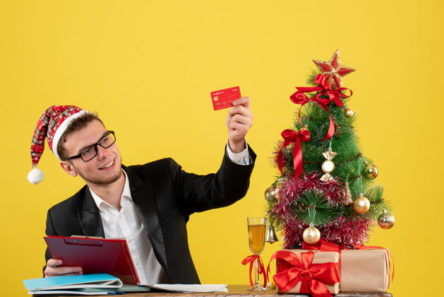 银行正面图：手持银行卡和纸条的男工人围着圣诞树 黄色的礼物抱着在周围男的