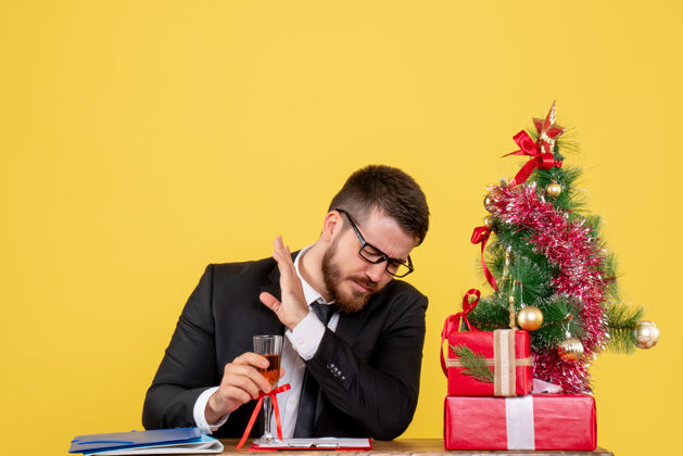 颜色正面图：桌子后面的男工人拿着礼物 黄色的圣诞树新郎工作人