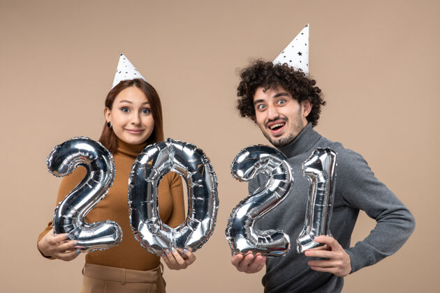 情侣快乐的年轻夫妇带着惊讶的表情 戴着新年礼帽 摆出一副摄影女孩和穿灰色衣服的男人的姿势男人姿势面部