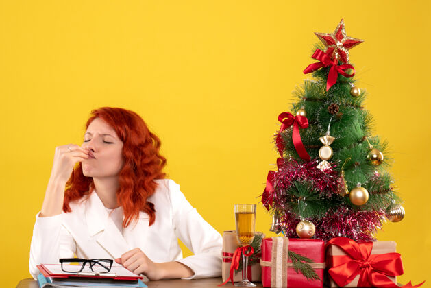 女性正面图：女医生坐在桌子后面 黄色桌子上放着圣诞礼物和圣诞树桌子医院礼物