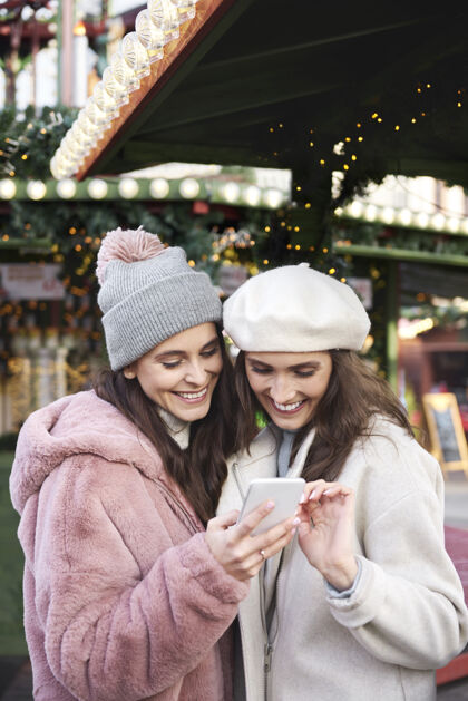 圣诞装饰两个朋友在圣诞集市上浏览手机短信女人衣服