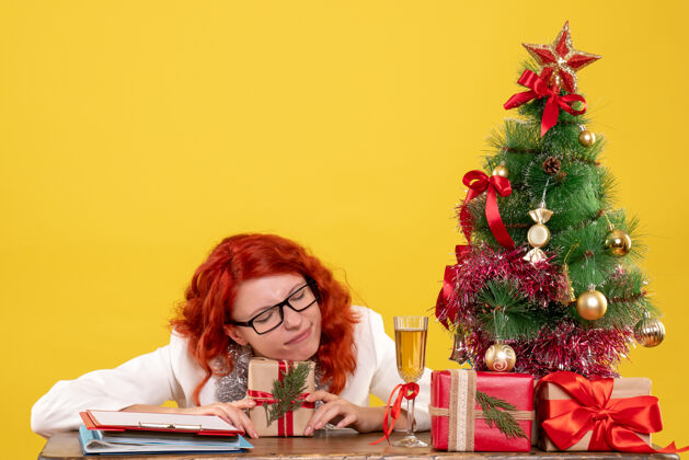 礼物前视图：女医生坐在桌子后面 黄色背景上有圣诞礼物人情感前面