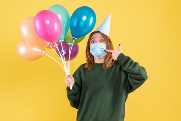 举行正面图戴面具的年轻女性手持五颜六色的气球女人气球气球