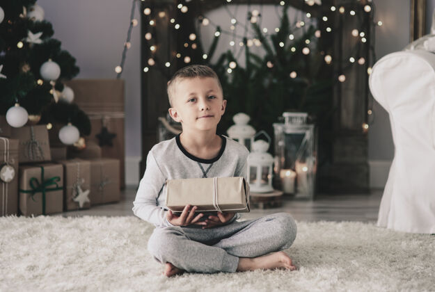 圣诞节小男孩拿着圣诞礼物坐在地毯上生活惊喜圣诞节