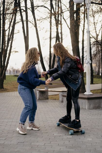 垂直两个女朋友在公园玩滑板在一起娱乐休闲