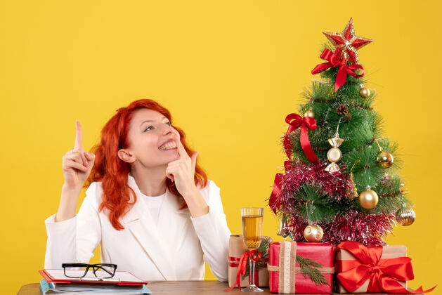 医院正面图：女医生坐在桌子后面 拿着圣诞礼物 黄色背景上的树情感礼物圣诞节