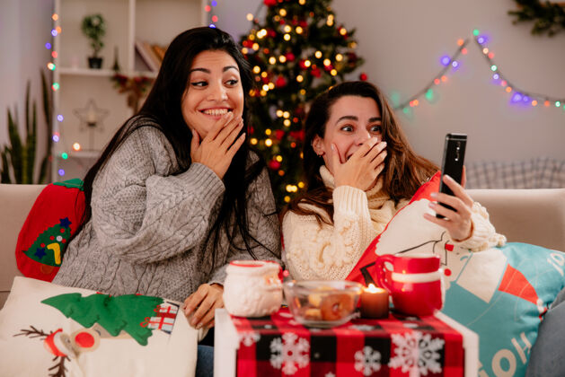 时间年轻漂亮的女孩们坐在扶手椅上看手机 在家里享受圣诞节时光印象深刻看年轻