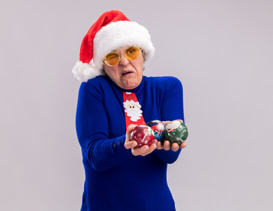 帽子戴着太阳眼镜 戴着圣诞帽 打着圣诞领带 手里拿着玻璃球饰物的恼怒的老妇人圣诞快乐玻璃女人