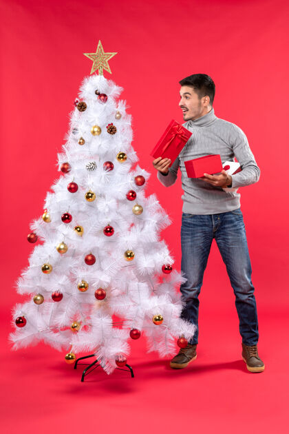衣服一个穿着灰色上衣的英俊的成年人站在装饰过的白色圣诞树旁的俯视图圣诞树礼物站着
